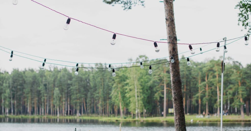 Wooden terrace with green trees and tables located near lake preparing for festive romantic party in nature under blue sky