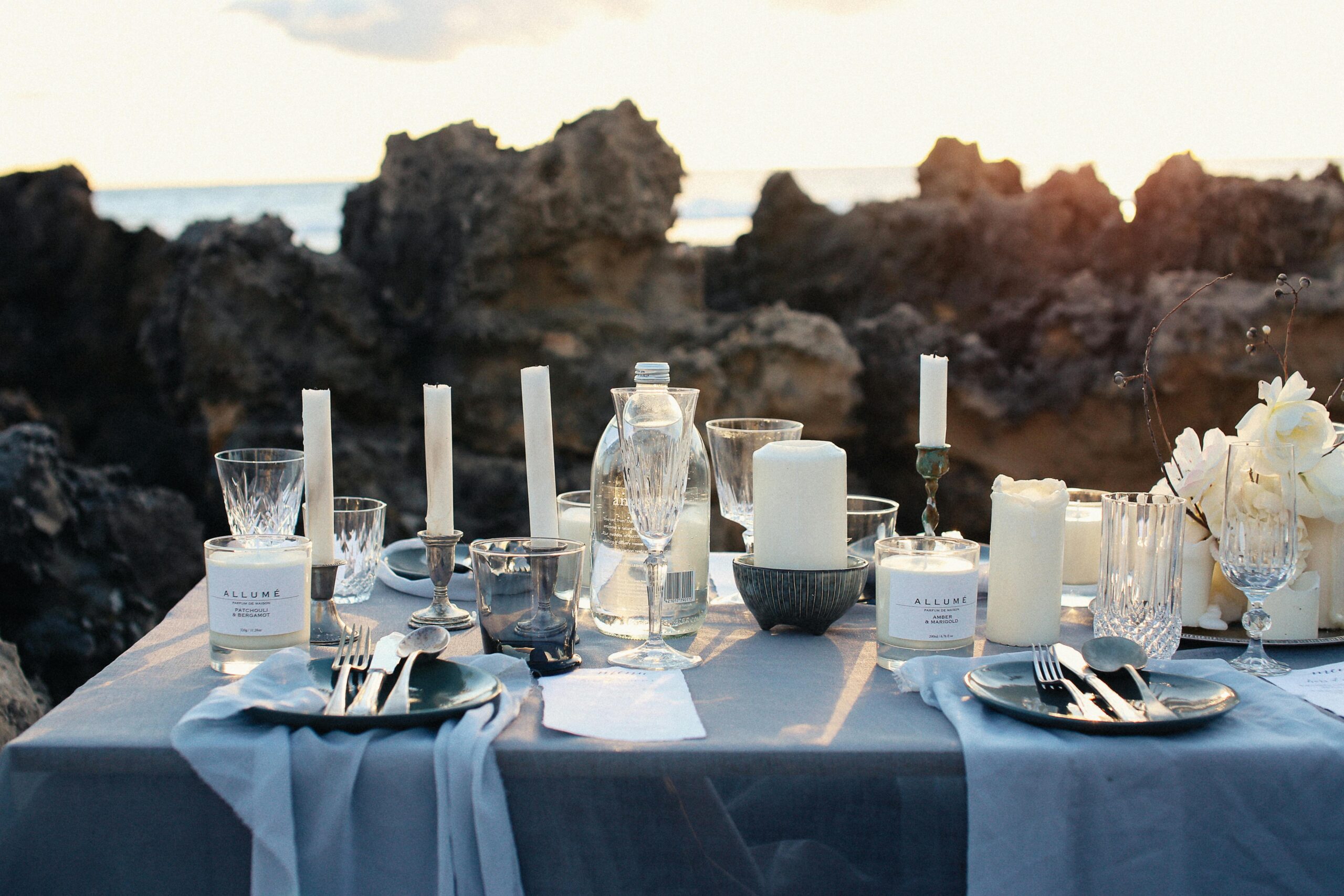 A luxurious table setting on a rocky beach with candles and elegant glassware, perfect for an outdoor dining experience.